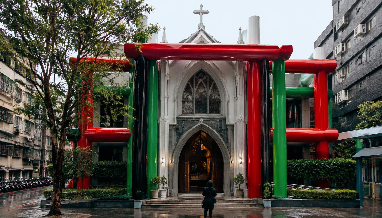 Photorealistic surreal photography of a beautiful Catholic church near cram schools on Nanyang Street, Taiwan, horizontal beams and columns made of glossy plastic-like material in fluorescent red, green, and deep black, an anonymous visitor hesitating at the entrance, subtly impossible architectural repetition, natural urban light, cinematic composition, no text, no lettering, no readable signage, no watermark.