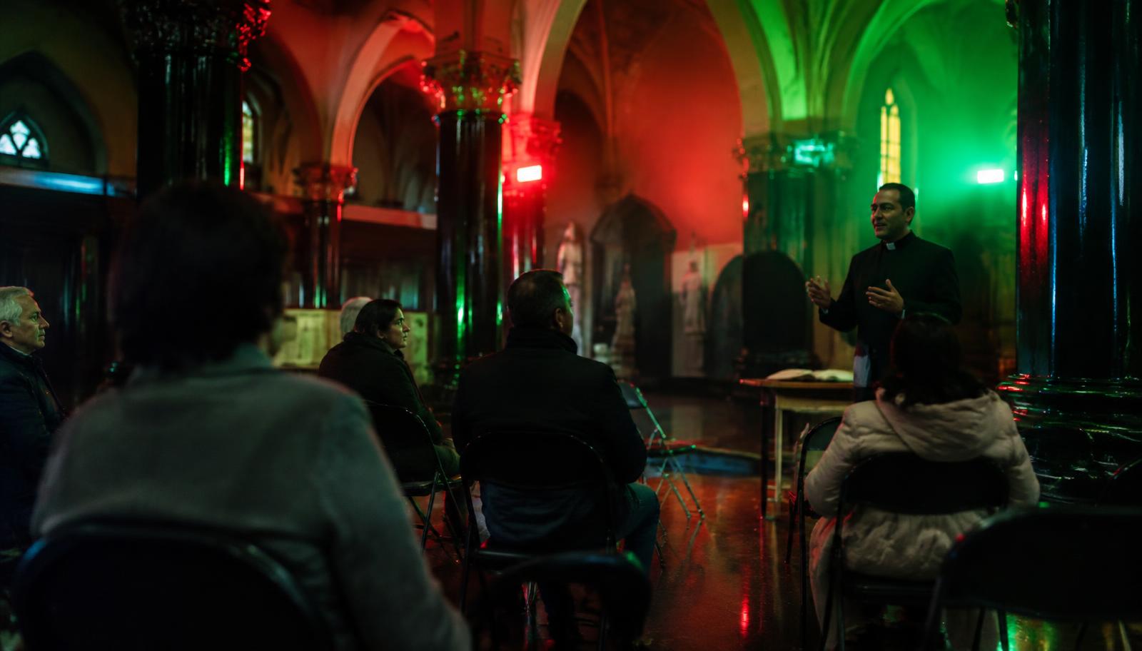 Photorealistic surreal photography inside a Catholic church arranged like a modest classroom, a pastor beginning a business lesson after prayer, friendly adult attendees listening quietly, fluorescent red and green light reflected from glossy black plastic-like columns, sacred architecture subtly merging with a cram school interior, realistic faces and materials, dreamlike spatial depth, no text, no lettering, no charts, no watermark.